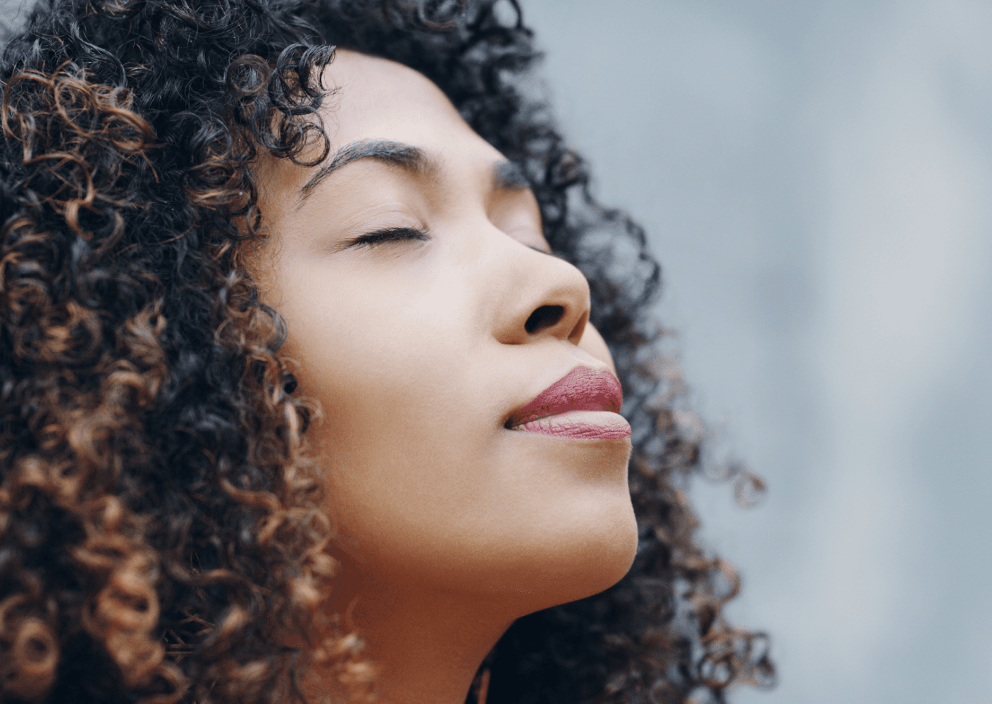 Photo of a woman with closed eyes enjoys a moment of calm and relaxation outdoors.