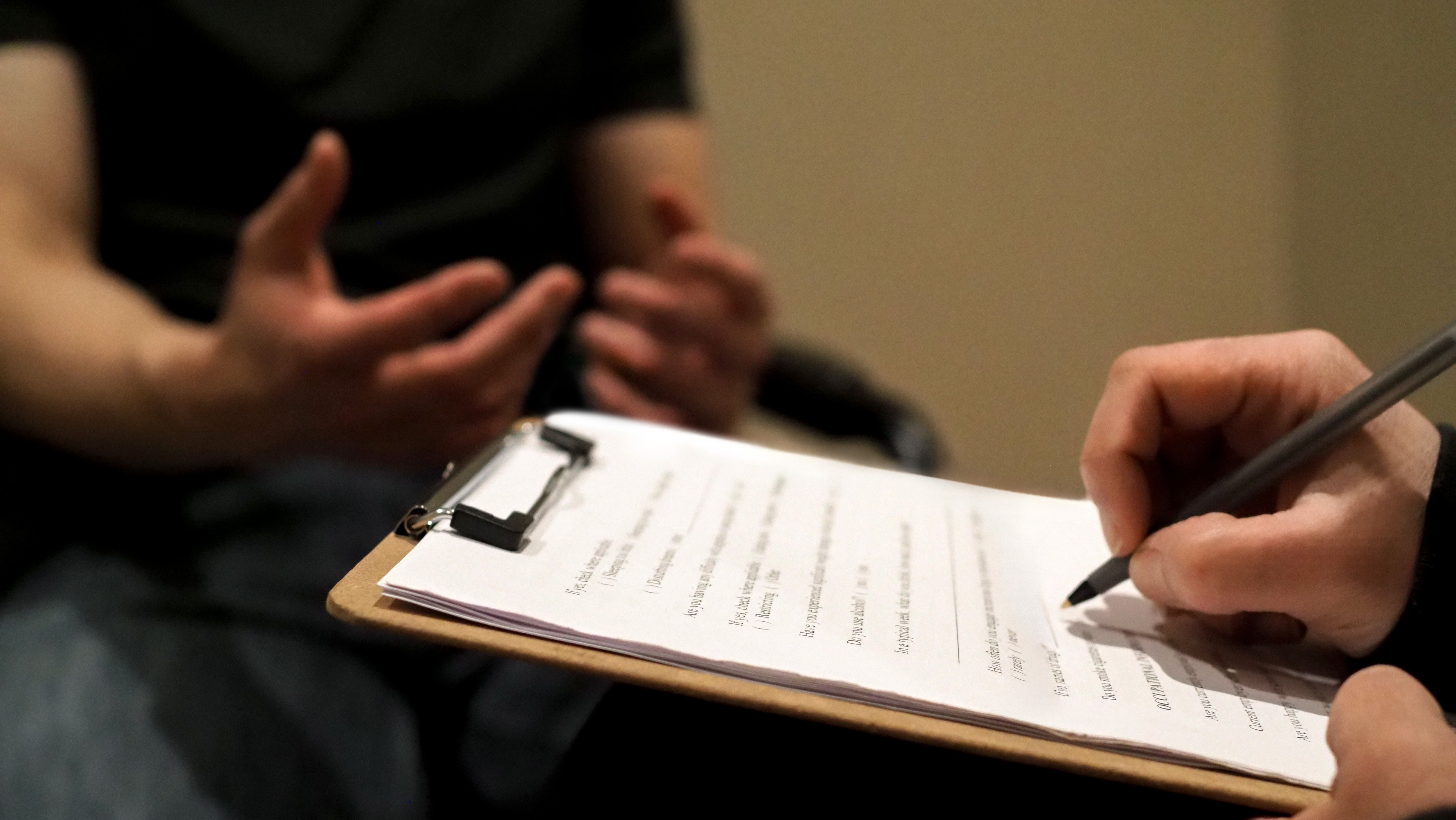 Photo of a therapist taking notes on a clipboard while listening to a client during a counseling session.