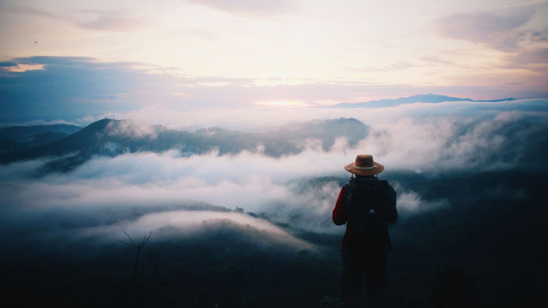 Silhouetted hiker overlooking misty mountain landscape at dawn, atmospheric landscape photograph.