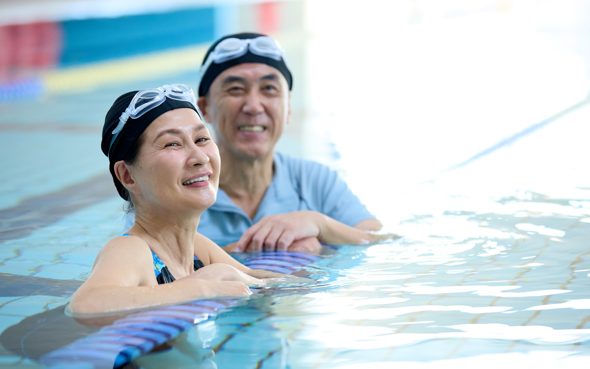 An older couple holding foam floats in a swimming pool.