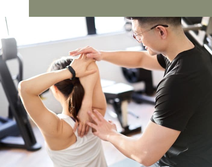 Photograph of a trainer assists a person stretching their arm in a gym setting.