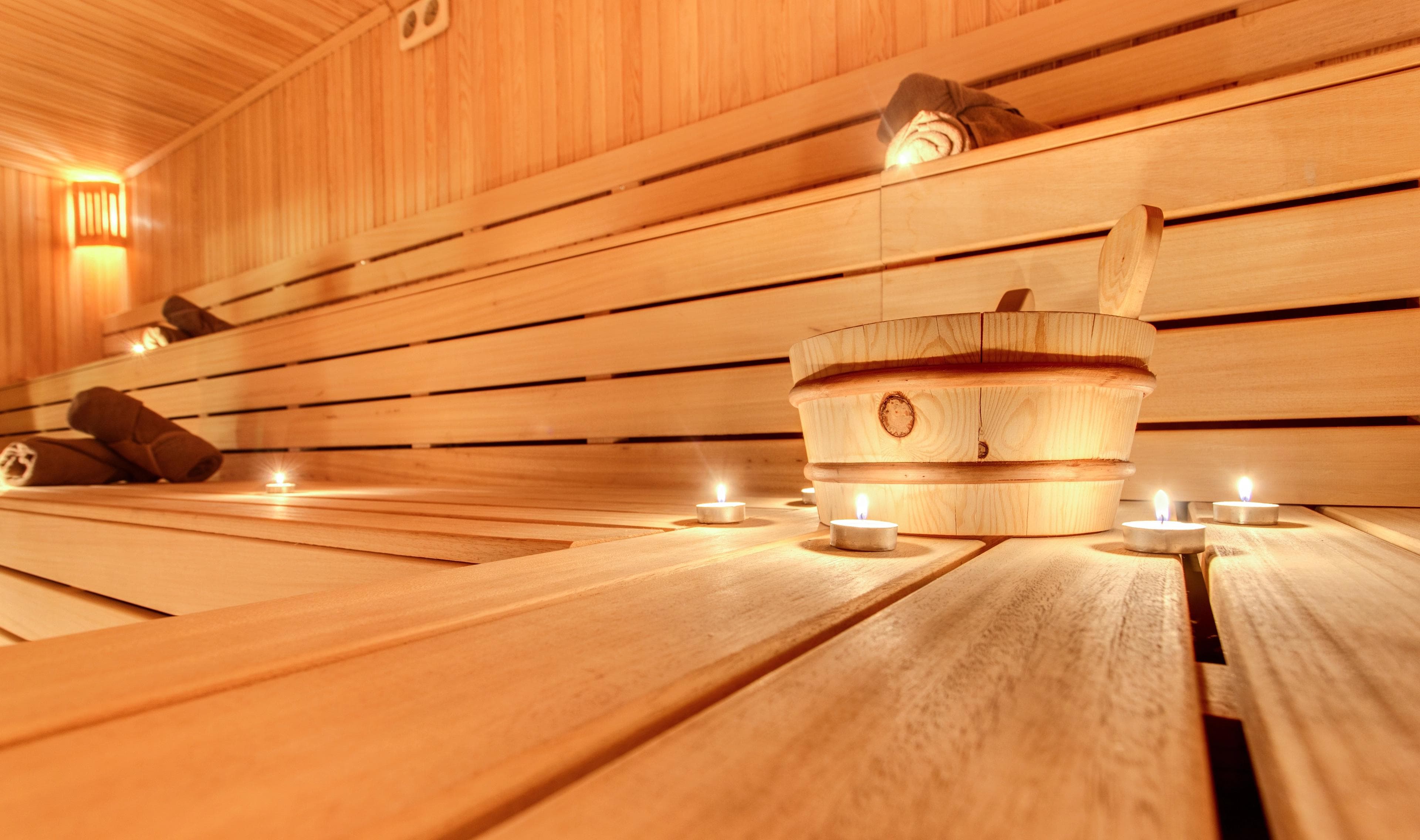 Interior view of a traditional wooden sauna with tiered benches and white towels, showing natural wood paneling and slat construction