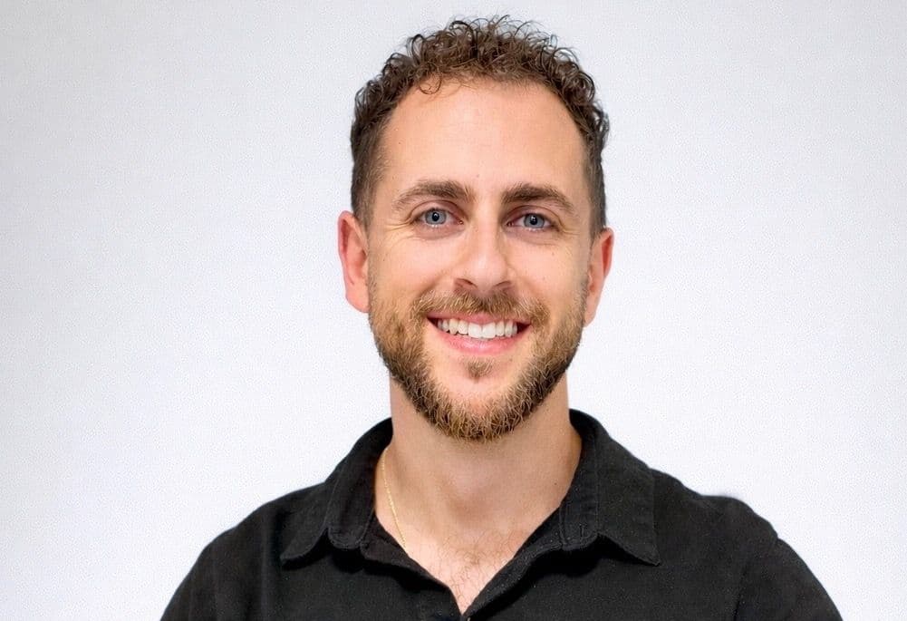 Headshot of Ariel Zohar smiling in a black shirt against a plain background.