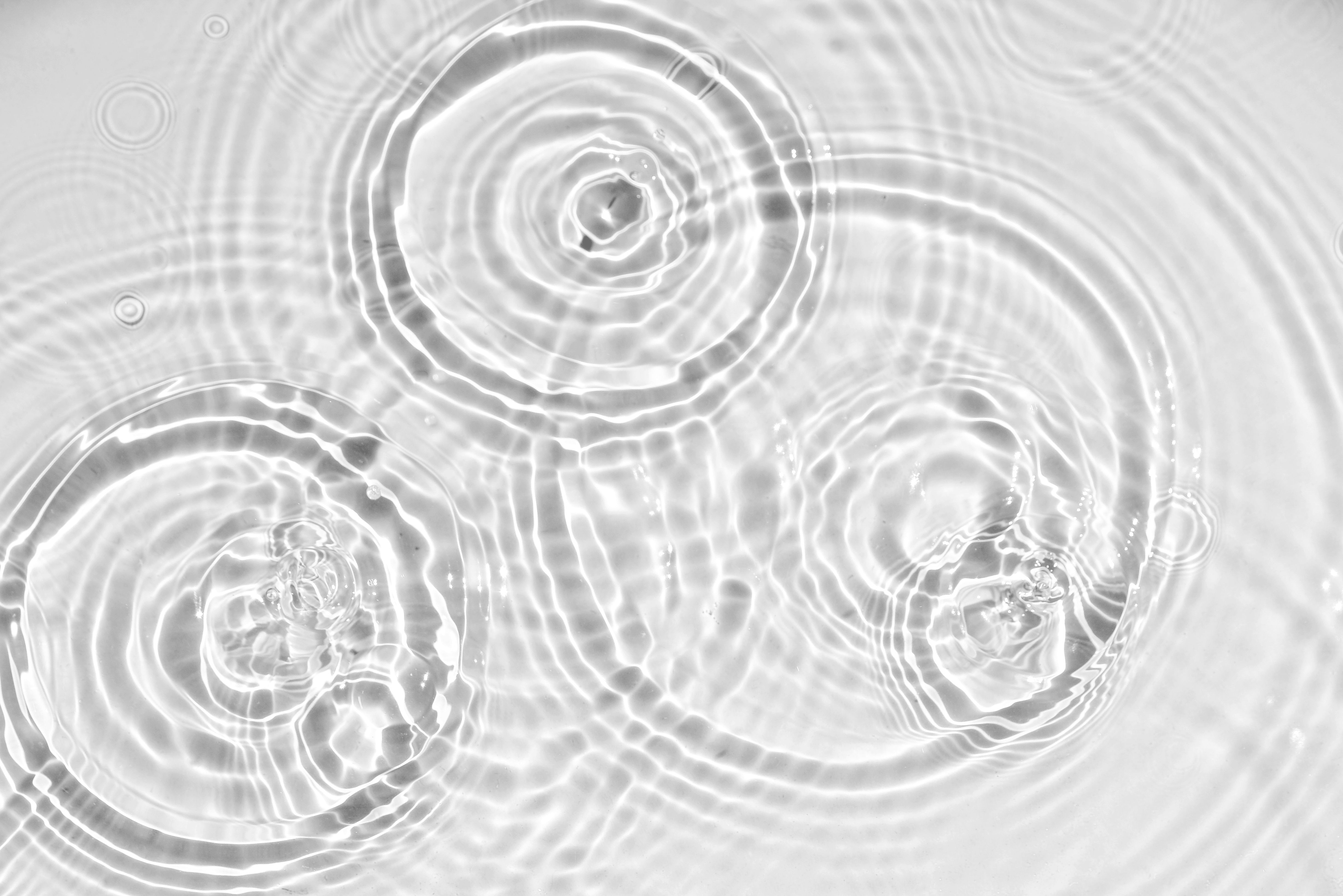 Photograph of circular ripples in water forming concentric rings, captured in black and white with high contrast showing detailed wave patterns.