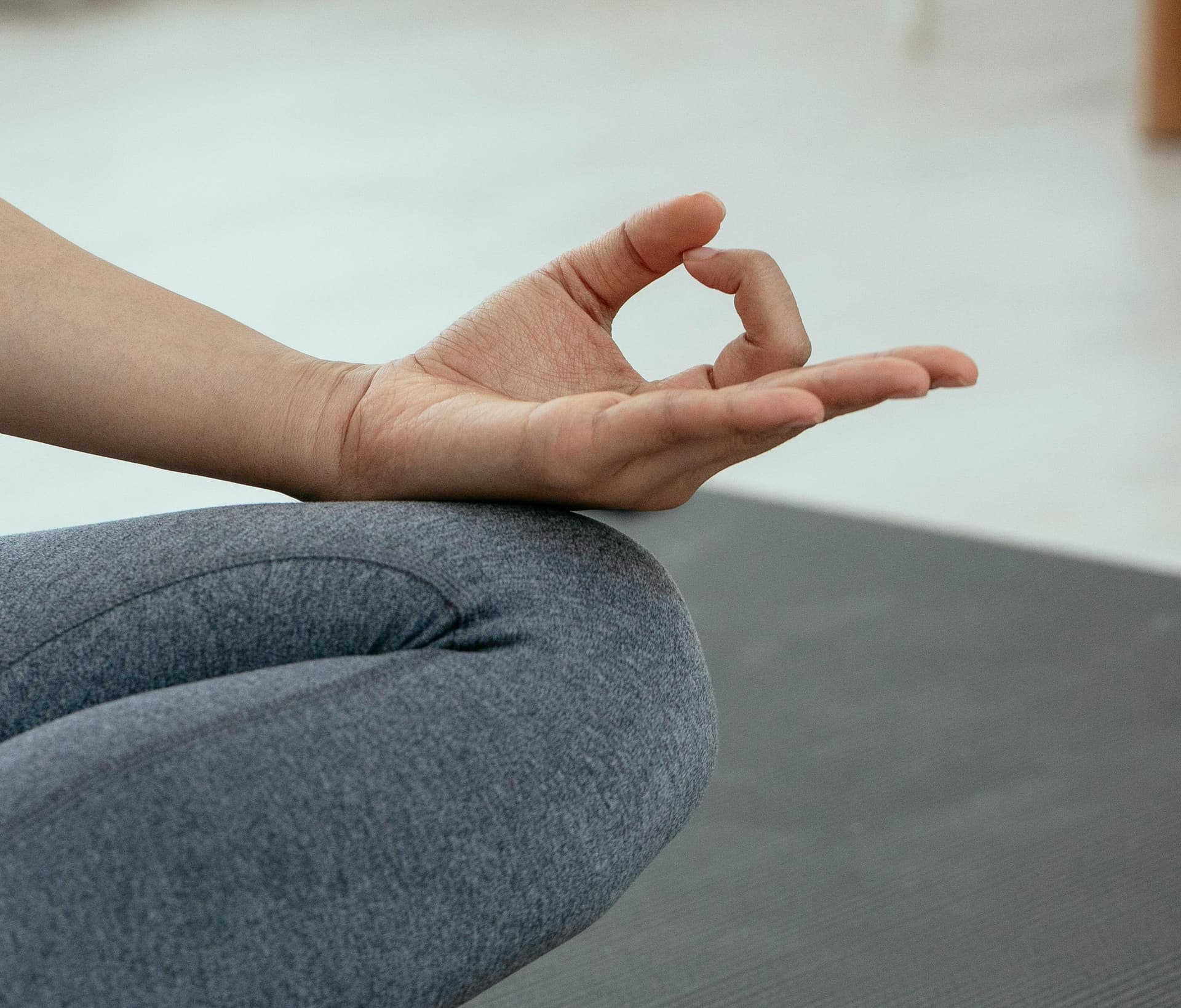 Close-up photo of a person sitting cross-legged in a meditative pose on a yoga mat, with one hand in a mudra gesture.
