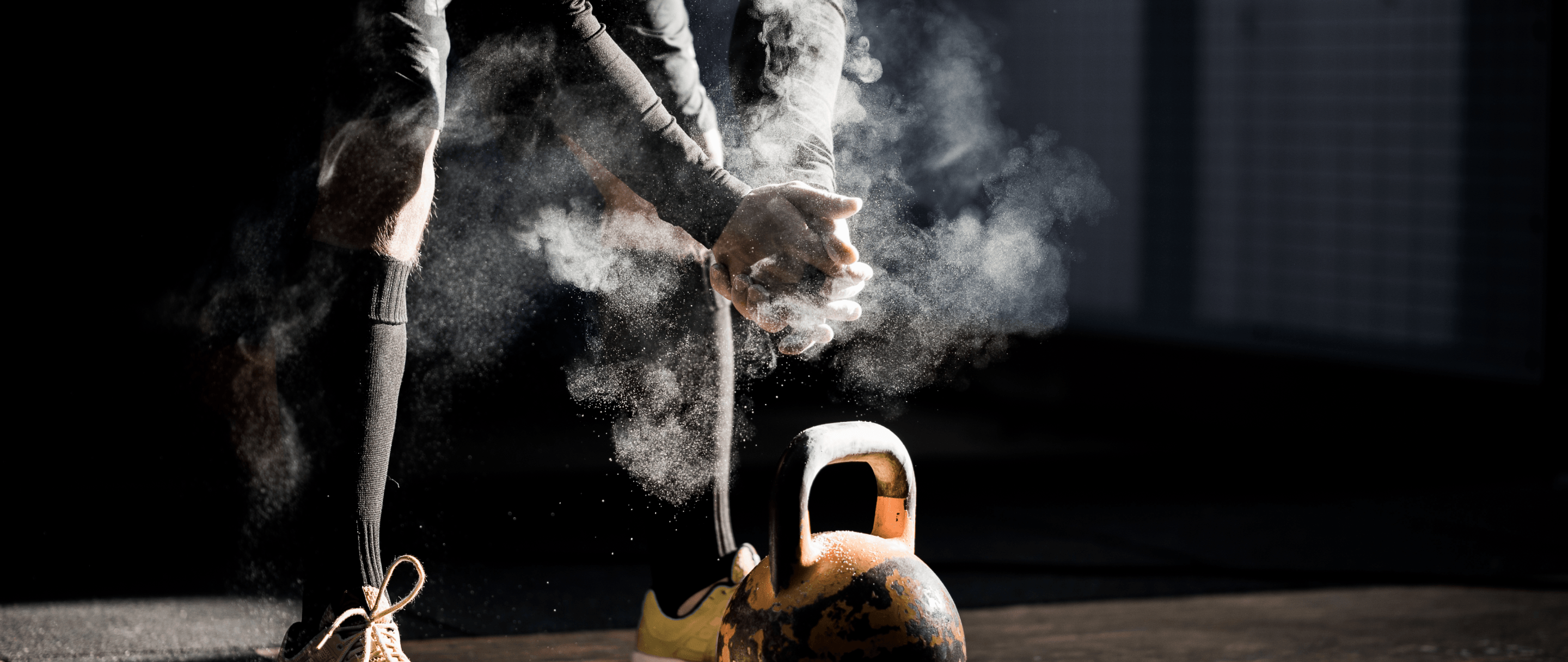 Photo of a person preparing for a kettlebell workout, with chalk dust in the air, in a dimly lit gym setting.
