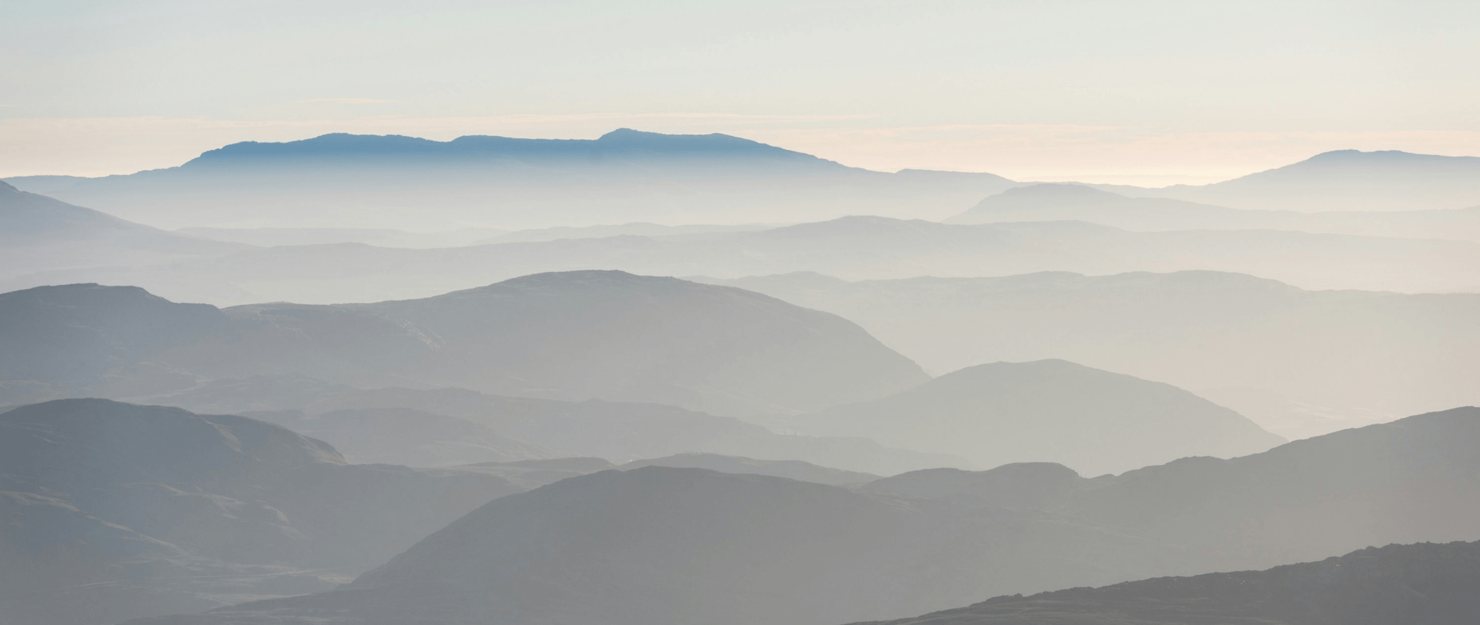 A serene photo of misty mountain layers under a soft sky, evoking a calm and tranquil atmosphere.