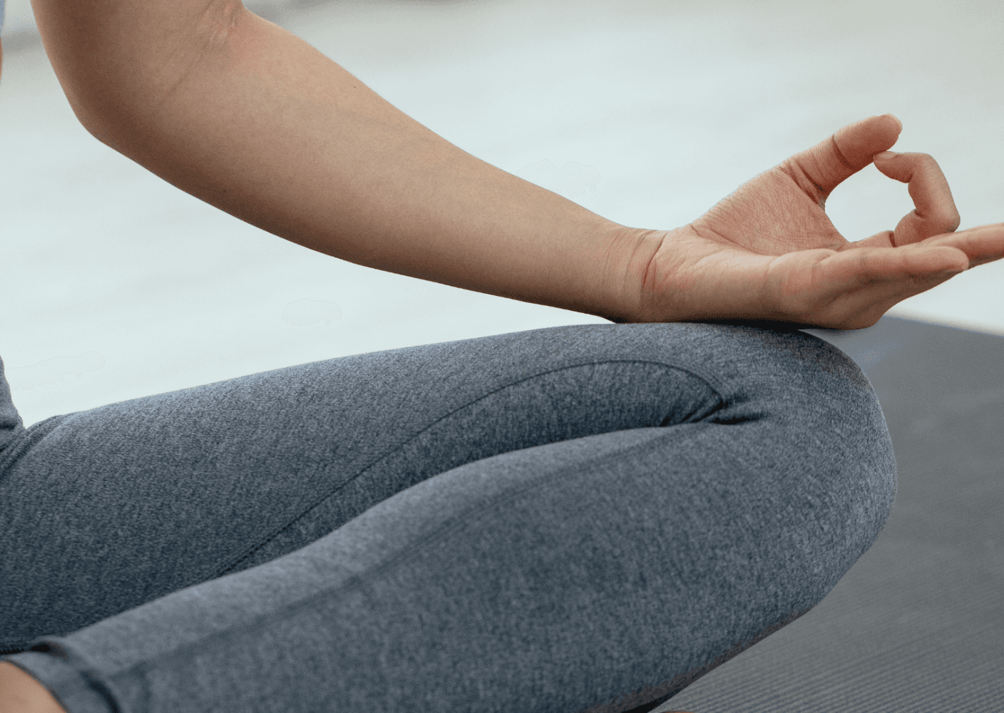 Close-up photo of a person sitting cross-legged in a meditative pose on a yoga mat, with one hand in a mudra gesture.