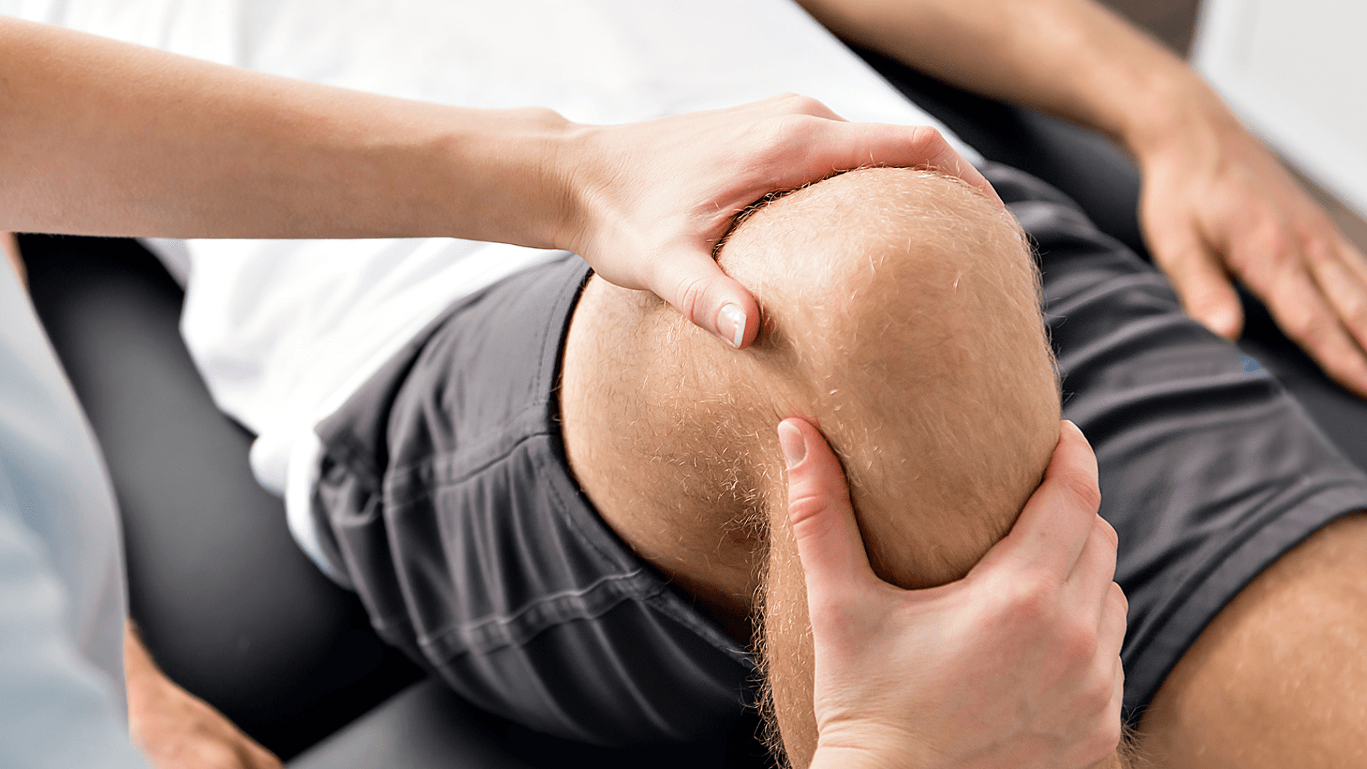 A photo showing a physical therapist applying pressure and support to a patient's knee during a therapy session.