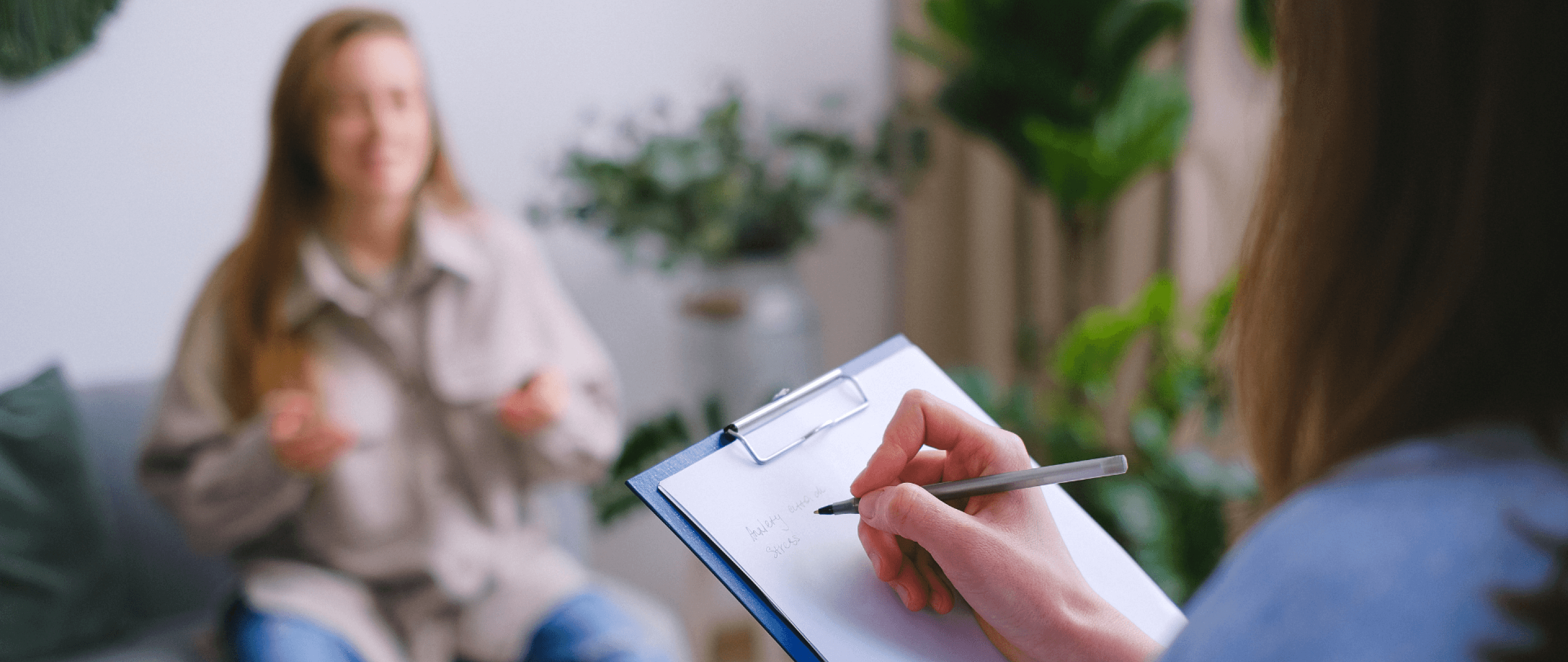 Photo of a therapist takes notes on a clipboard while listening to a client during a counseling session.