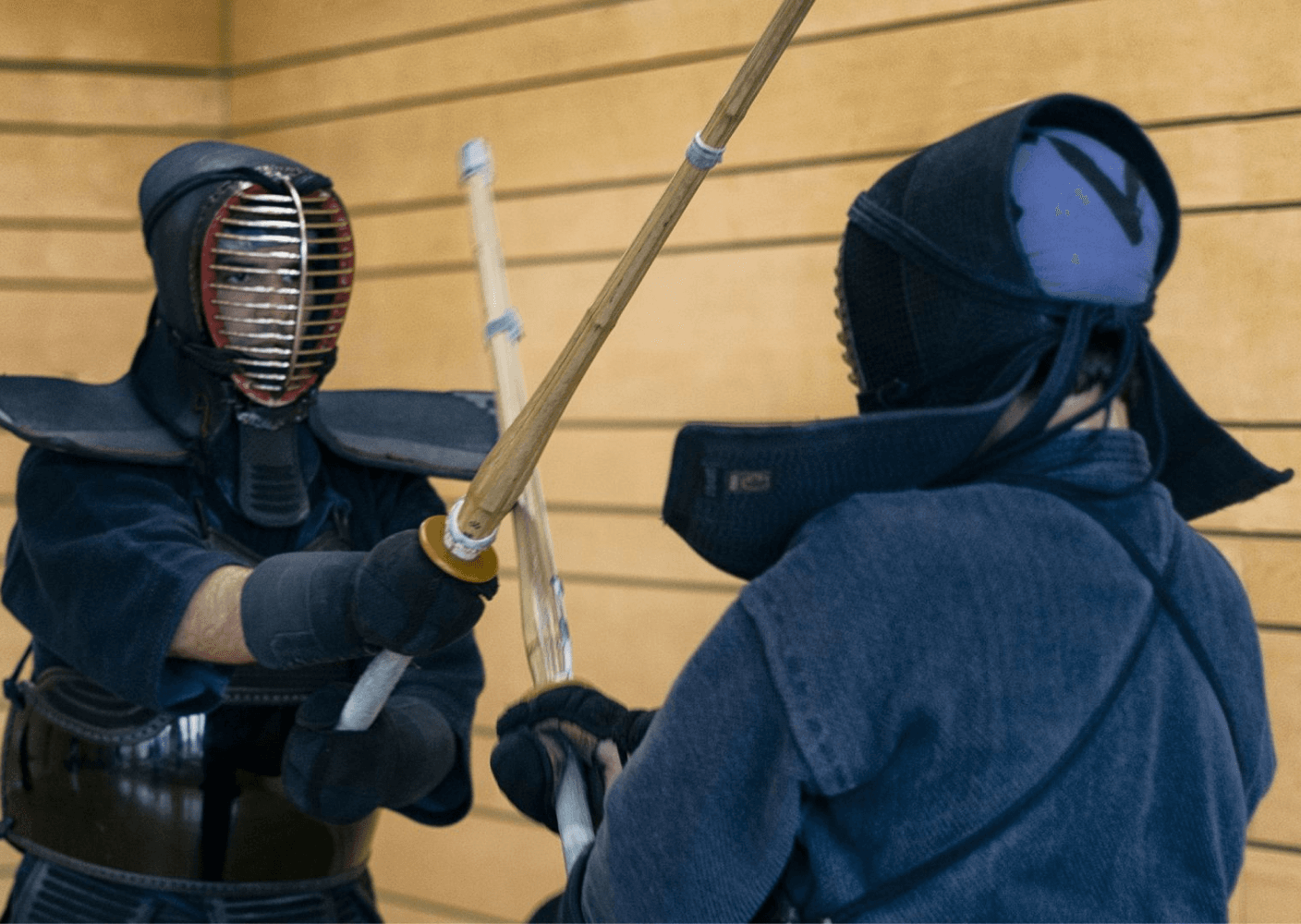 Photo of two kendo practitioners in protective gear sparring with bamboo swords in a dojo setting.